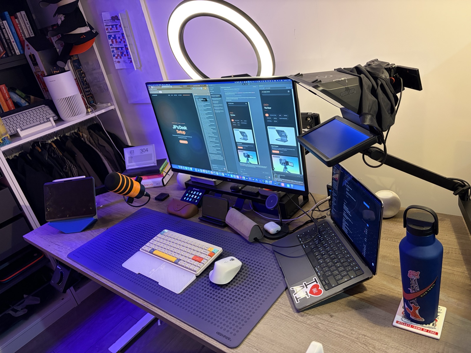 Side angle of desk showing monitor, teleprompter, microphone, and laptop